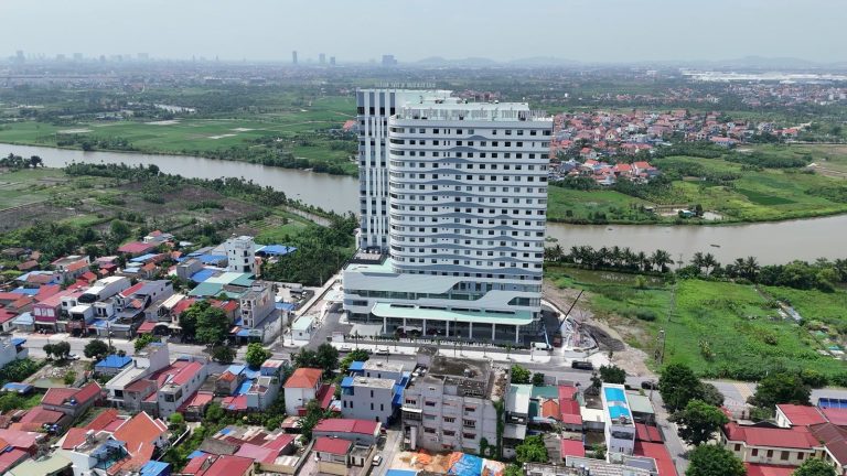 Toàn cảnh Bệnh viện Đa khoa Quốc tế Thủy Nguyên 19 tầng nhìn từ flycam tháng 9/2026, sông Trịnh chảy phía sau, khu dân cư Thủy Sơn bao quanh
