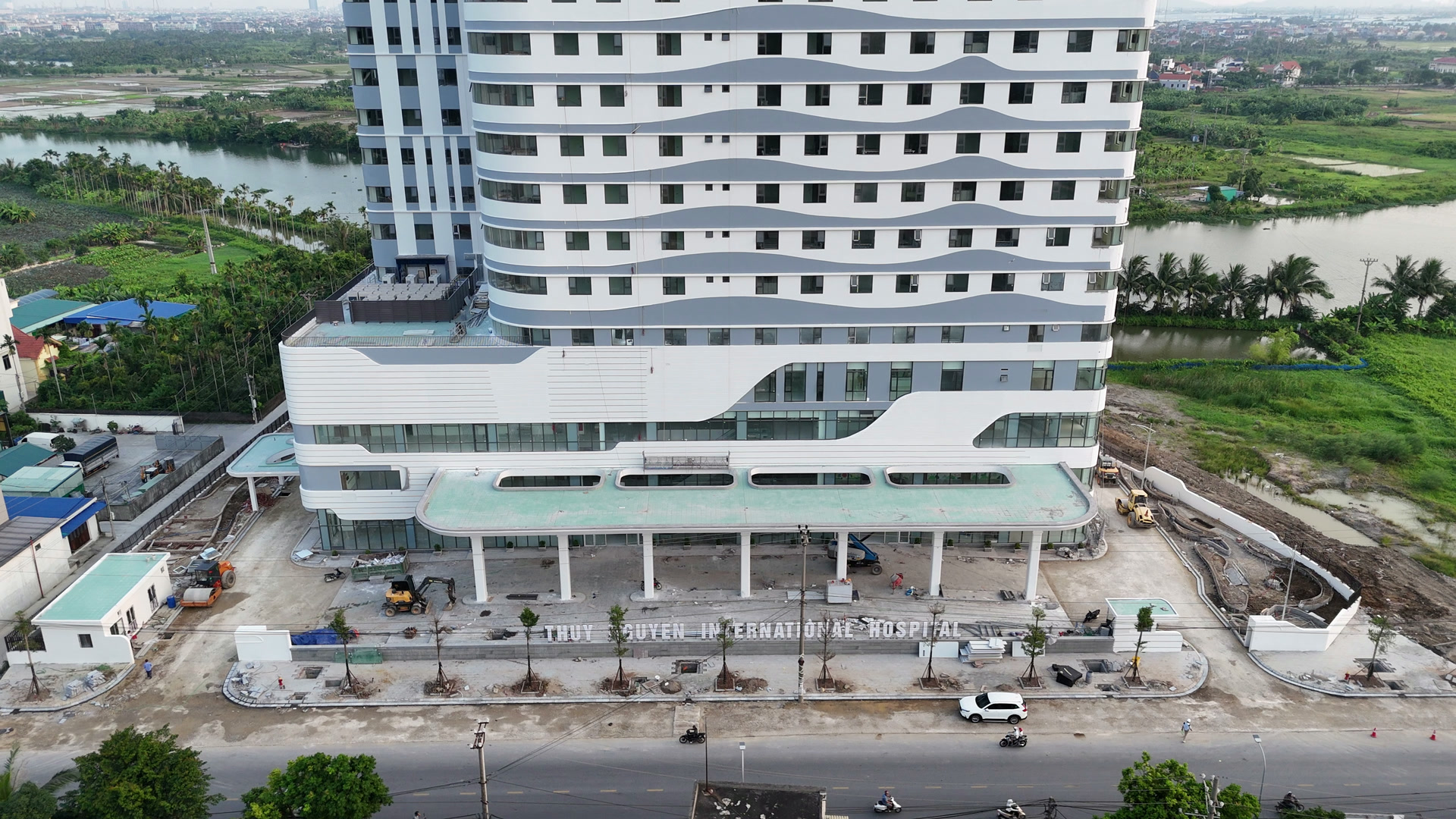 Mặt trước Bệnh viện Đa khoa Quốc tế Thủy Nguyên với mái che sảnh chính đã hình thành, phía trước vẫn còn vật liệu và phần sân chưa hoàn thiện