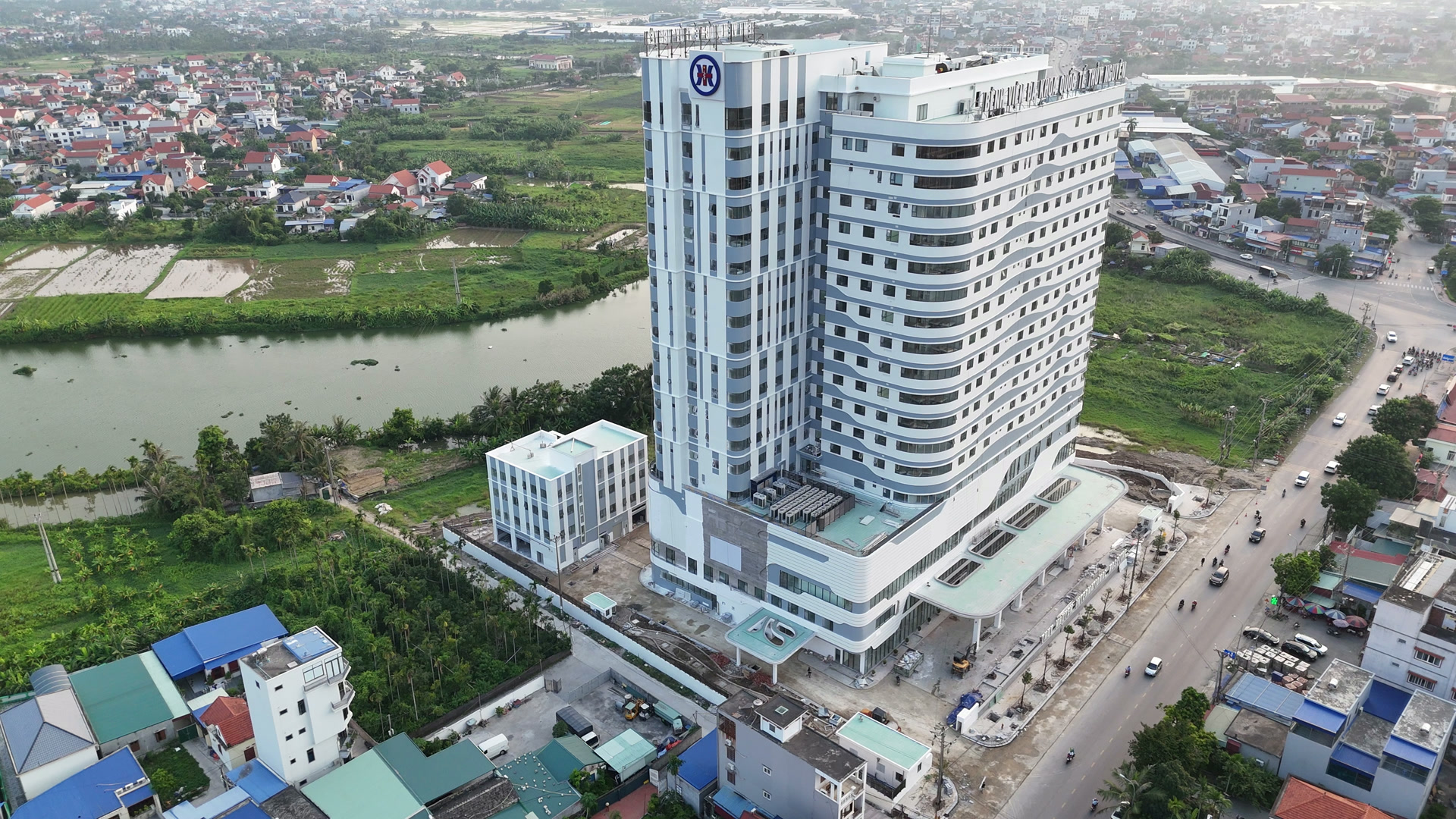 Toàn cảnh Bệnh viện Đa khoa Quốc tế Thủy Nguyên tháng 7/2026, toà nhà cao tầng màu trắng xám đã hoàn thiện mặt ngoài, biển tên đã gắn trên mái