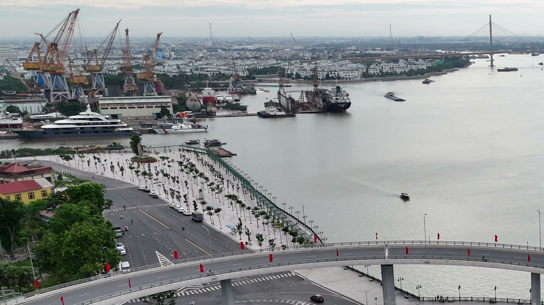 Nhà máy đóng tàu với dàn cần cẩu và các tàu đang neo sửa chữa nằm sát mép sông Cấm, đối diện là dải đường dạo ven sông đã trồng cây