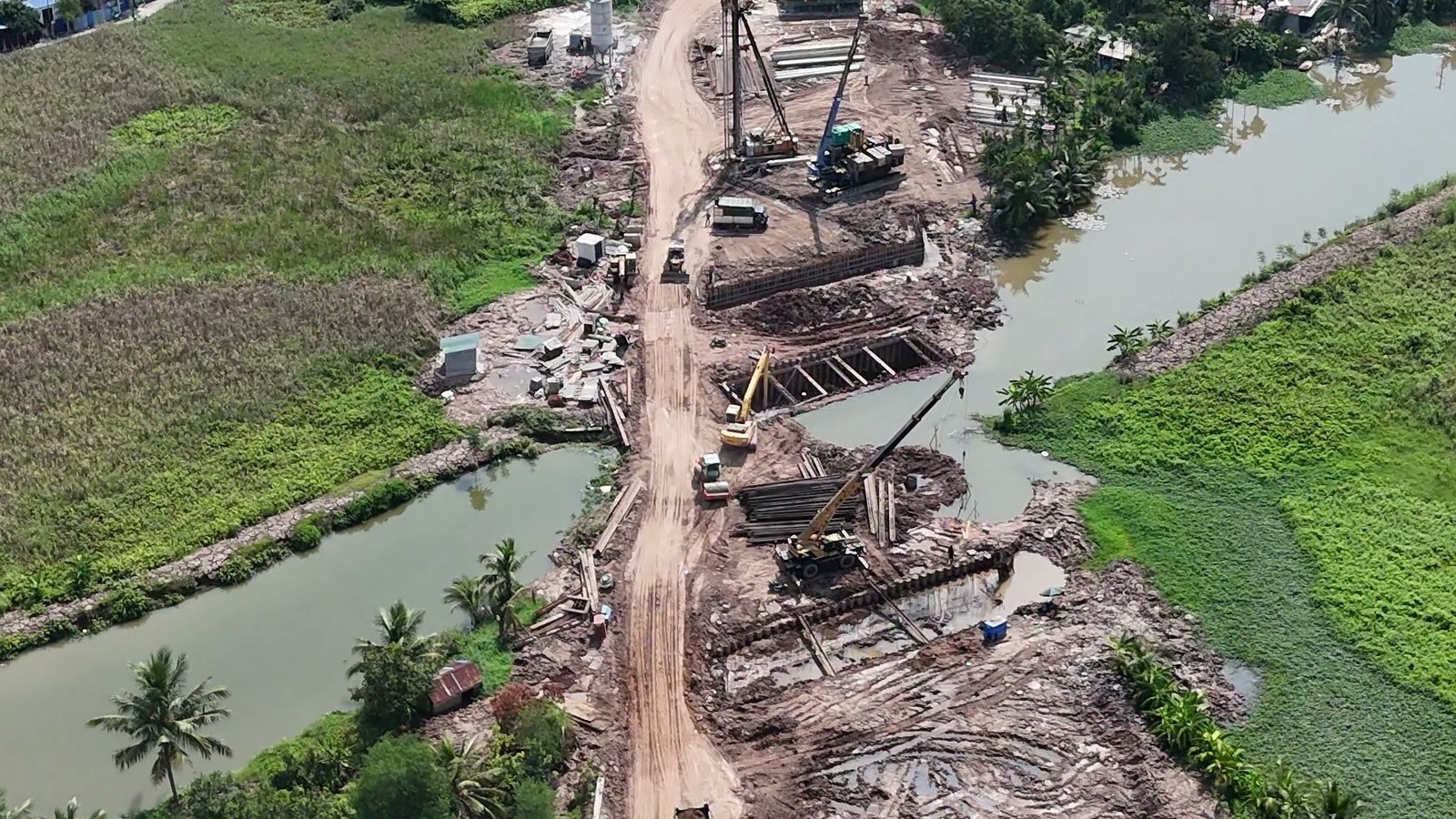 Chỗ đường 2,4km cắt ngang con kênh hồi tháng 8/2026, mấy hố đào sát bờ kênh quây cừ thép có thanh chống ngang, máy đóng cọc và cần cẩu đứng cạnh