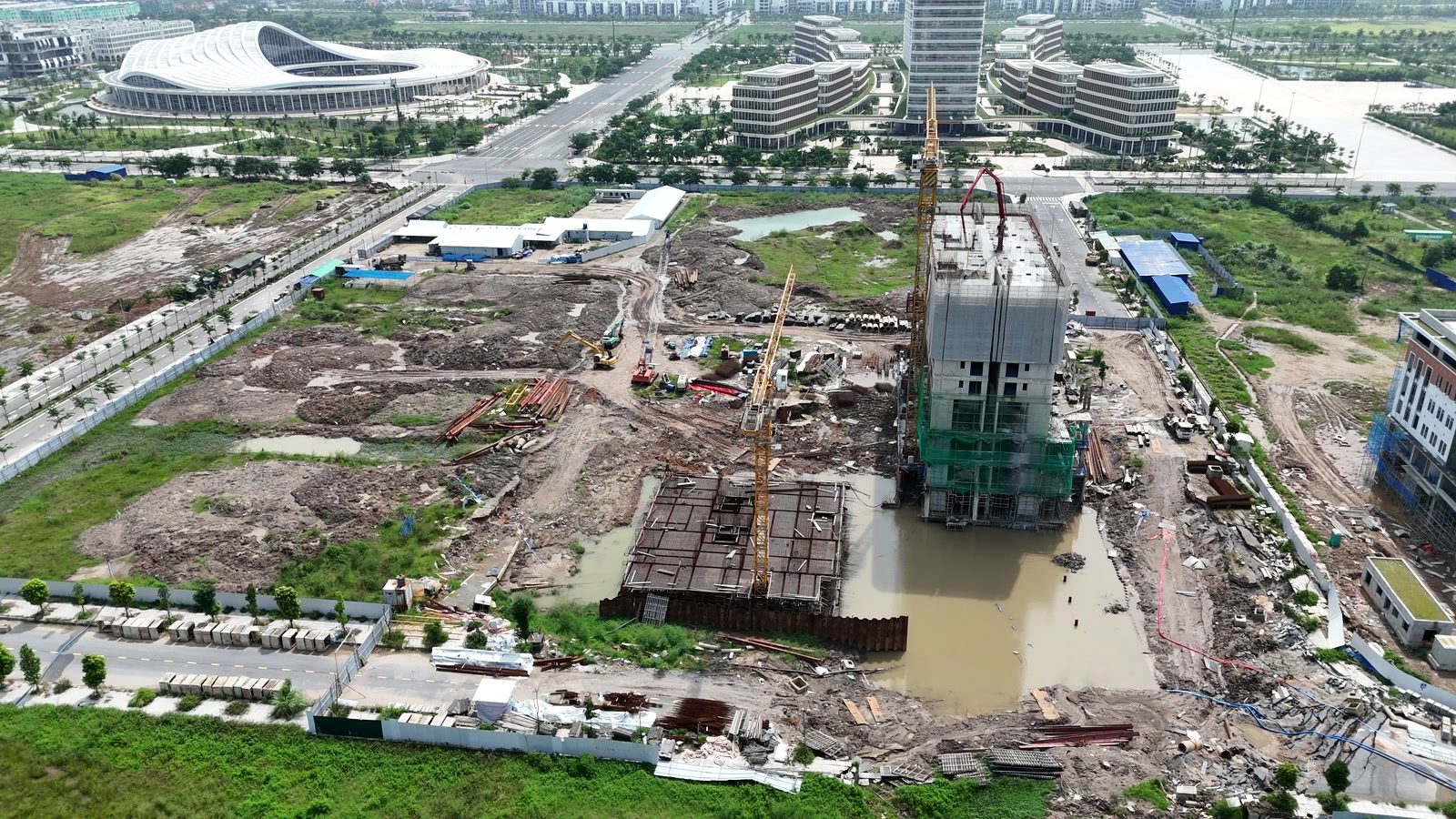 Công trường Central Point Hải Phòng, một khối nhà đang lên tầng phủ bạt với cần bơm bê tông vươn tới, ngay cạnh là hố hầm lớn đã đổ xong đáy và đọng nước mưa