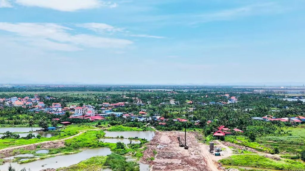 Nền đường đất màu nâu đỏ mới đắp chạy qua giữa ruộng và ao, hai bên là cây xanh và nhà dân, đường 2,4km Đỗ Mười ra đảo Vũ Yên tháng 5/2026