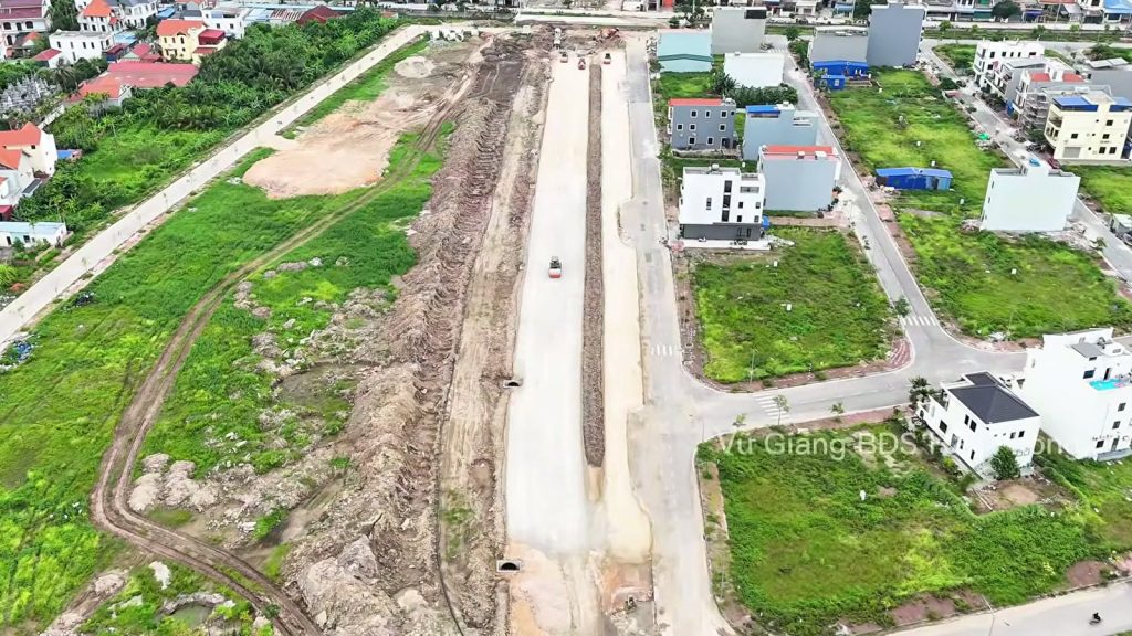 Nền đường đất rộng chạy thẳng giữa các khu nhà mới xây và bãi cỏ, đường 2,4km Đỗ Mười ra đảo Vũ Yên tháng 6/2026