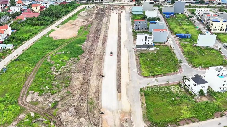 Nền đường đất rộng chạy thẳng giữa các khu nhà mới xây và bãi cỏ, đường 2,4km Đỗ Mười ra đảo Vũ Yên tháng 6/2026