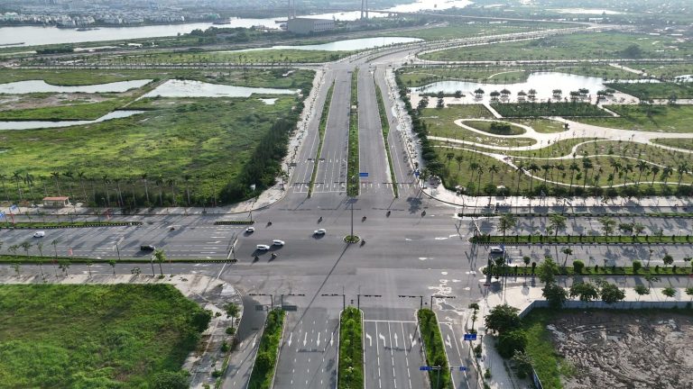 Đường Đông Tây Bắc Sông Cấm nhìn dọc tuyến, mặt đường chia làm bốn phần song song ngăn bởi ba dải cây xanh, hai bên còn nhiều đất trống
