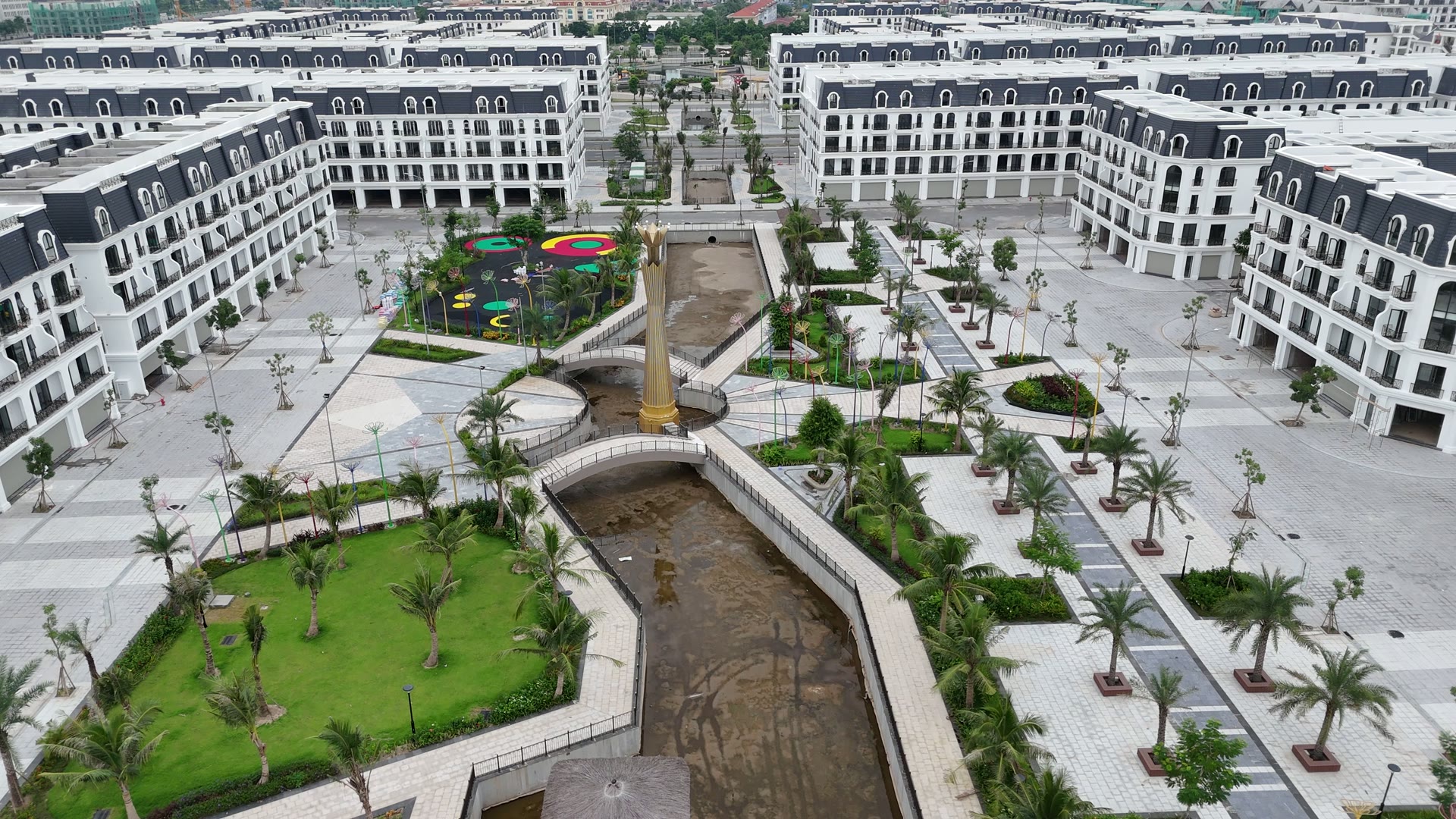 Công viên giữa khu Hoàng Tử ở Hoàng Huy New City với sân chơi trẻ em mặt sân nhiều màu, tháp vàng và con kênh chạy giữa, hai bên là các dãy nhà đã xây xong