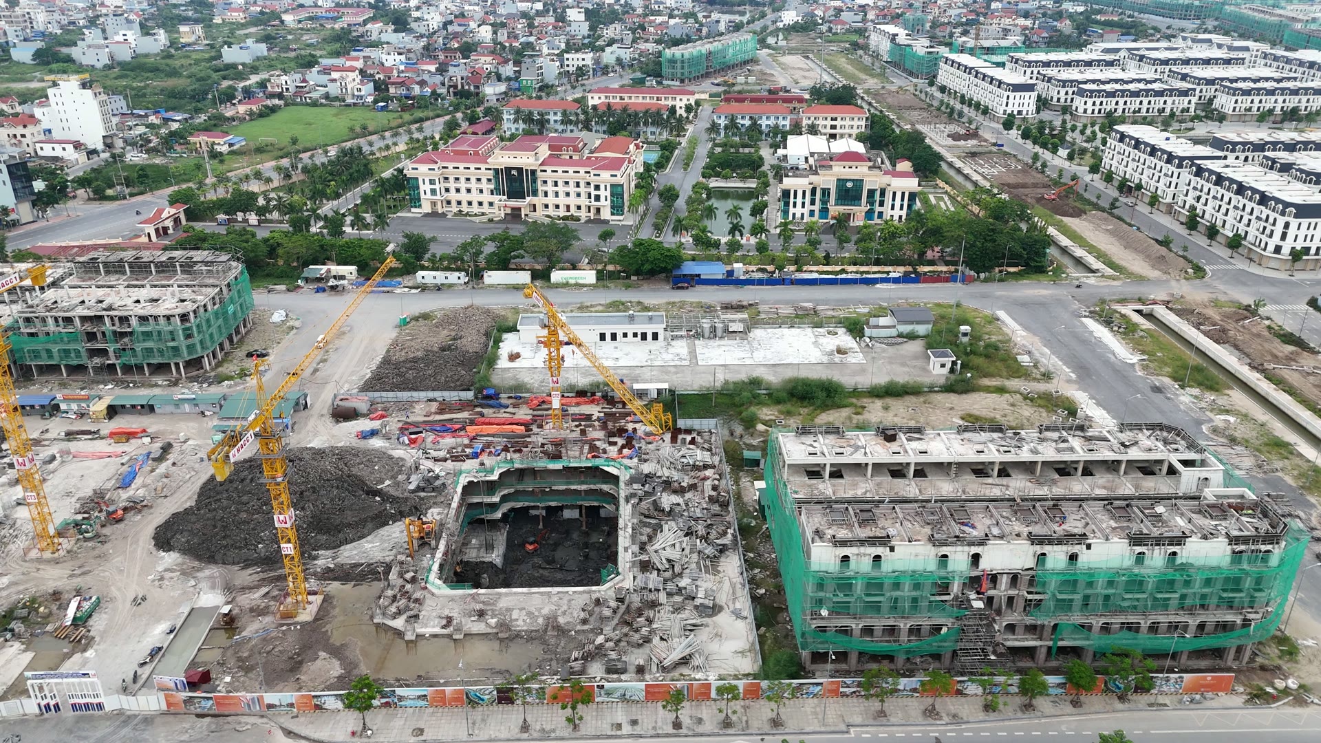 Hố tầng hầm một tòa căn hộ Sky Light ở Hoàng Huy New City, thành hố quây kín, hai cẩu tháp màu vàng dựng bên cạnh, đống đất đá xám chất cao và dãy nhà thấp tầng còn bọc lưới xanh phía sau