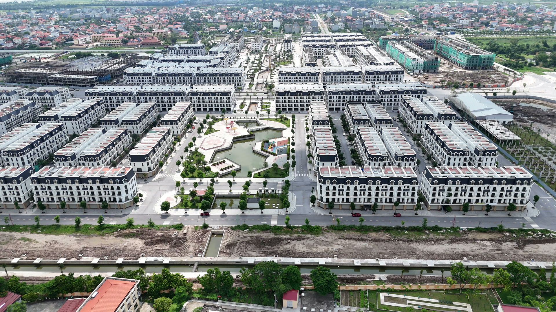 Toàn cảnh khu thấp tầng Hoàng Huy New City tháng 7/2026 nhìn từ trên cao, nhiều dãy nhà đã sơn trắng hoàn thiện, ở giữa là trục công viên và hồ cảnh quan