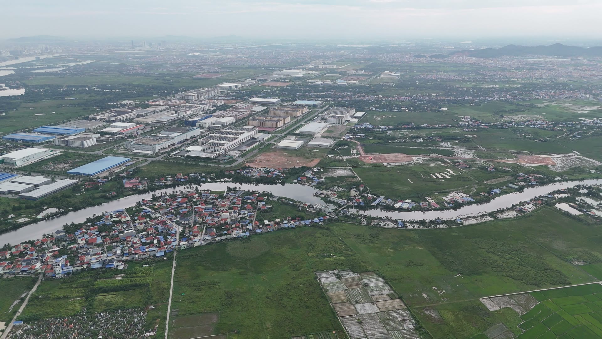 Khu nhà máy mái trắng mái xanh của khu công nghiệp VSIP Hải Phòng nằm bên kia một con sông uốn khúc, bên này là làng xóm ven sông và ruộng xanh