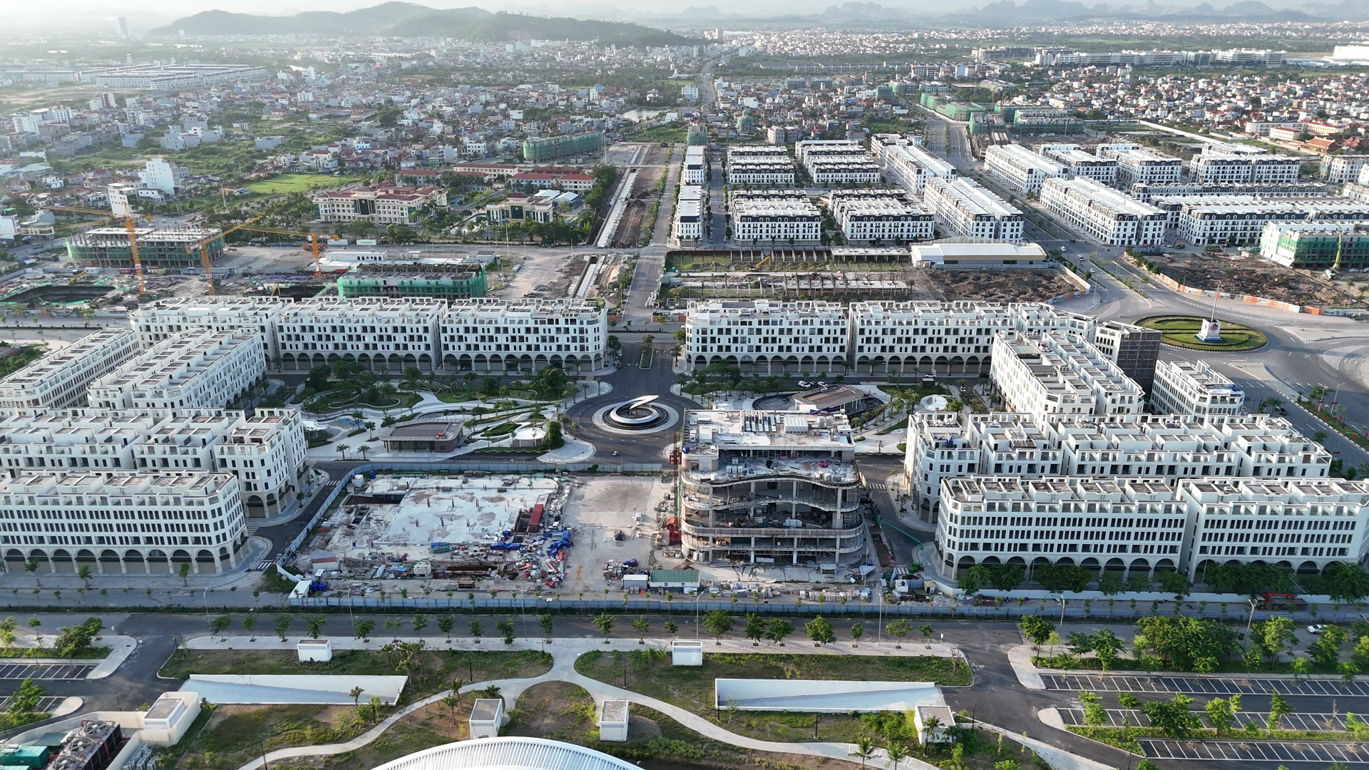 The Centric nhìn từ trên cao với các dãy shophouse trắng bao quanh, ở giữa là khối nhà đang thi công và các trục đường lớn của Bắc Sông Cấm