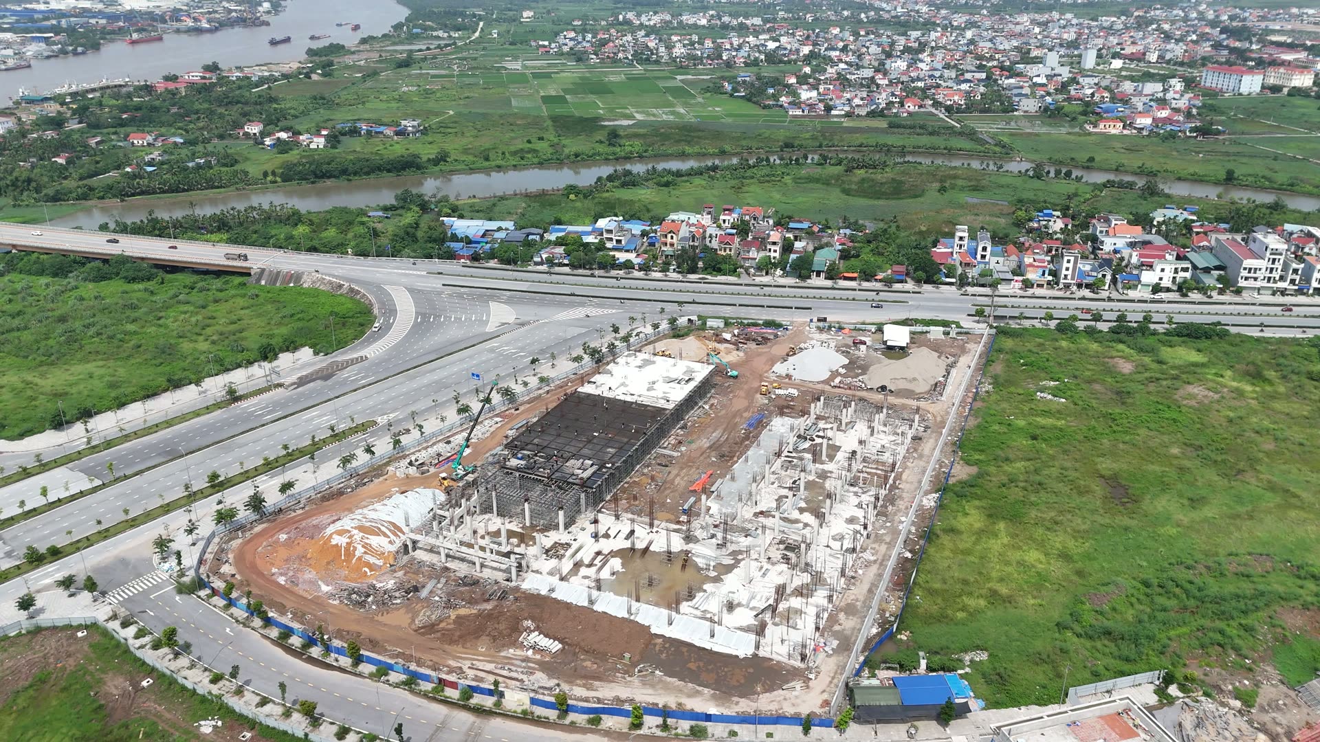 Một công trình lớn đang thi công phần móng và sàn tầng một bên trục đường lớn ở Bắc Sông Cấm, phía sau là khu dân cư và sông Cấm