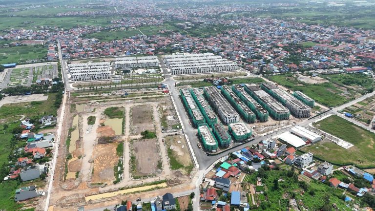 Toàn cảnh Vlasta Thủy Nguyên nhìn từ flycam tháng 8/2026, các dãy nhà đã sơn trắng nằm cạnh những dãy còn phủ lưới xanh và phần đất chưa xây