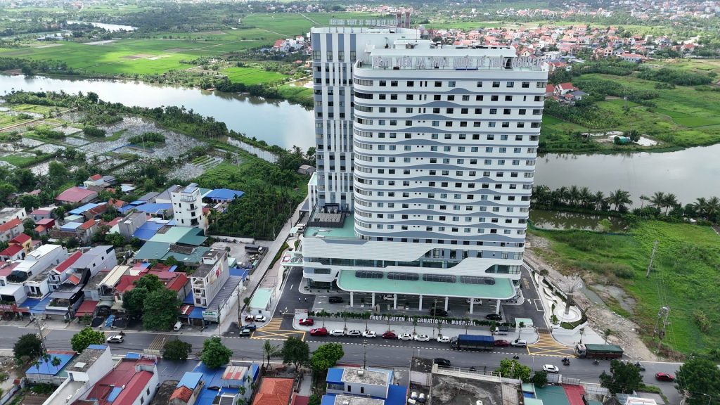 Bệnh viện Đa khoa Quốc tế Thủy Nguyên nhìn từ trên cao, toà nhà 19 tầng nằm sát mặt đường giữa khu dân cư, phía sau là sông Trịnh và đồng ruộng