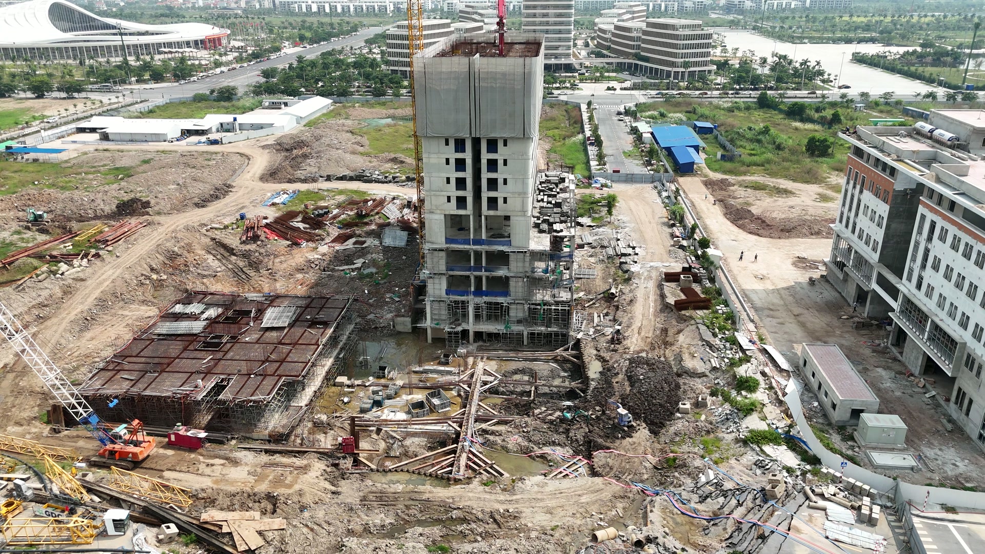 Công trường Central Point ở Bắc Sông Cấm, khối nhà cao tầng đang lên phần trên phủ bạt, bên trái là mặt hầm đã đan kín thép sàn, phía trước là một hố đào có thanh chống xiên ngang và máy làm dưới đáy