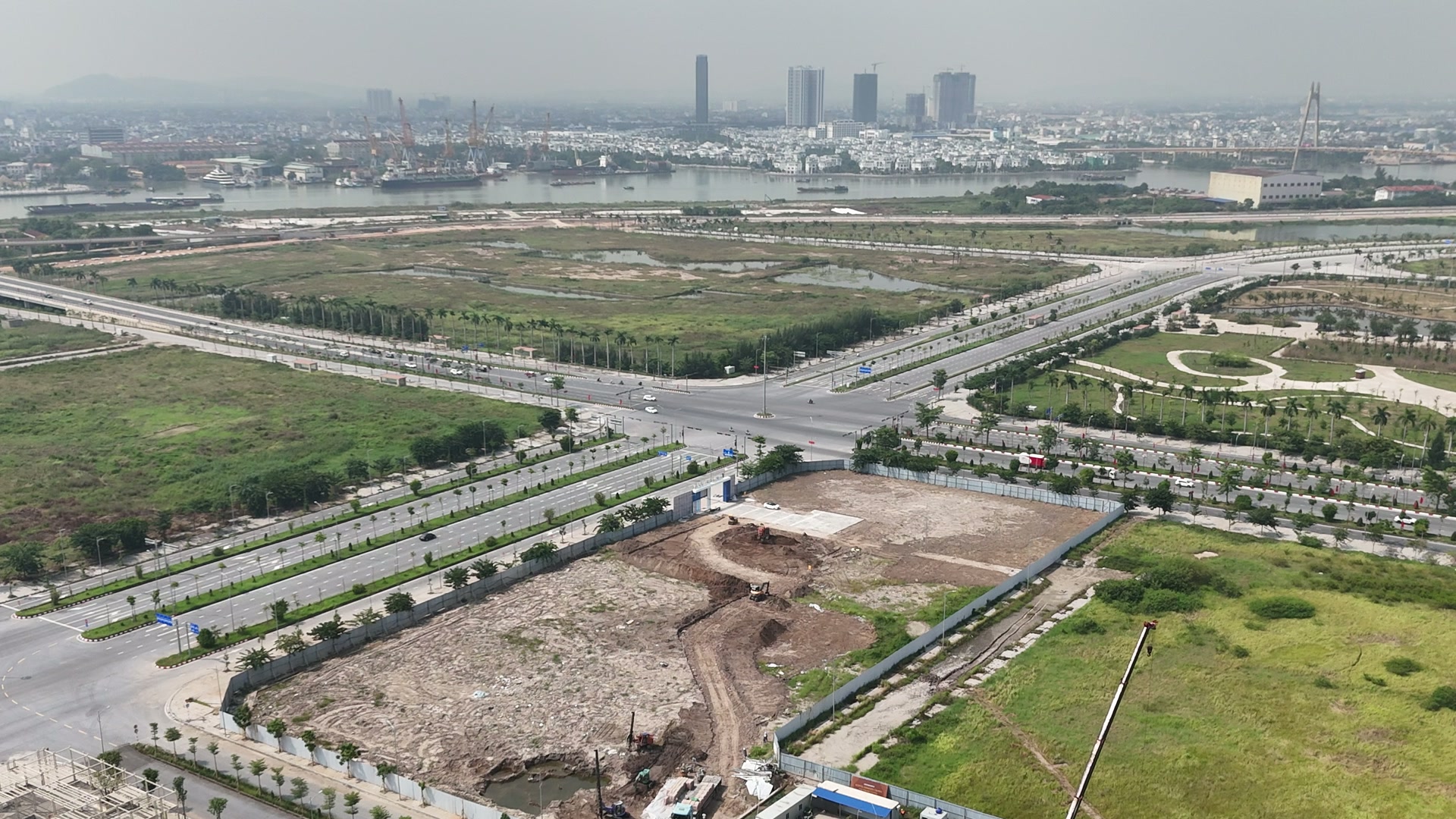 Lô đất Doji 75 Complex ở phía dưới khung, giáp hai đường nhiều làn có dải cây xanh giữa đường, phía xa là sông Cấm, bên kia sông là nội thành Hải Phòng với mấy toà nhà cao và một cây cầu dây văng
