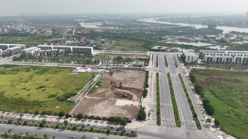 Lô đất Doji 75 Complex quây tôn trắng bên trục đường Đỗ Mười nhiều làn, máy xúc đang làm trong lô, phía xa là sông Cấm và khu cảng