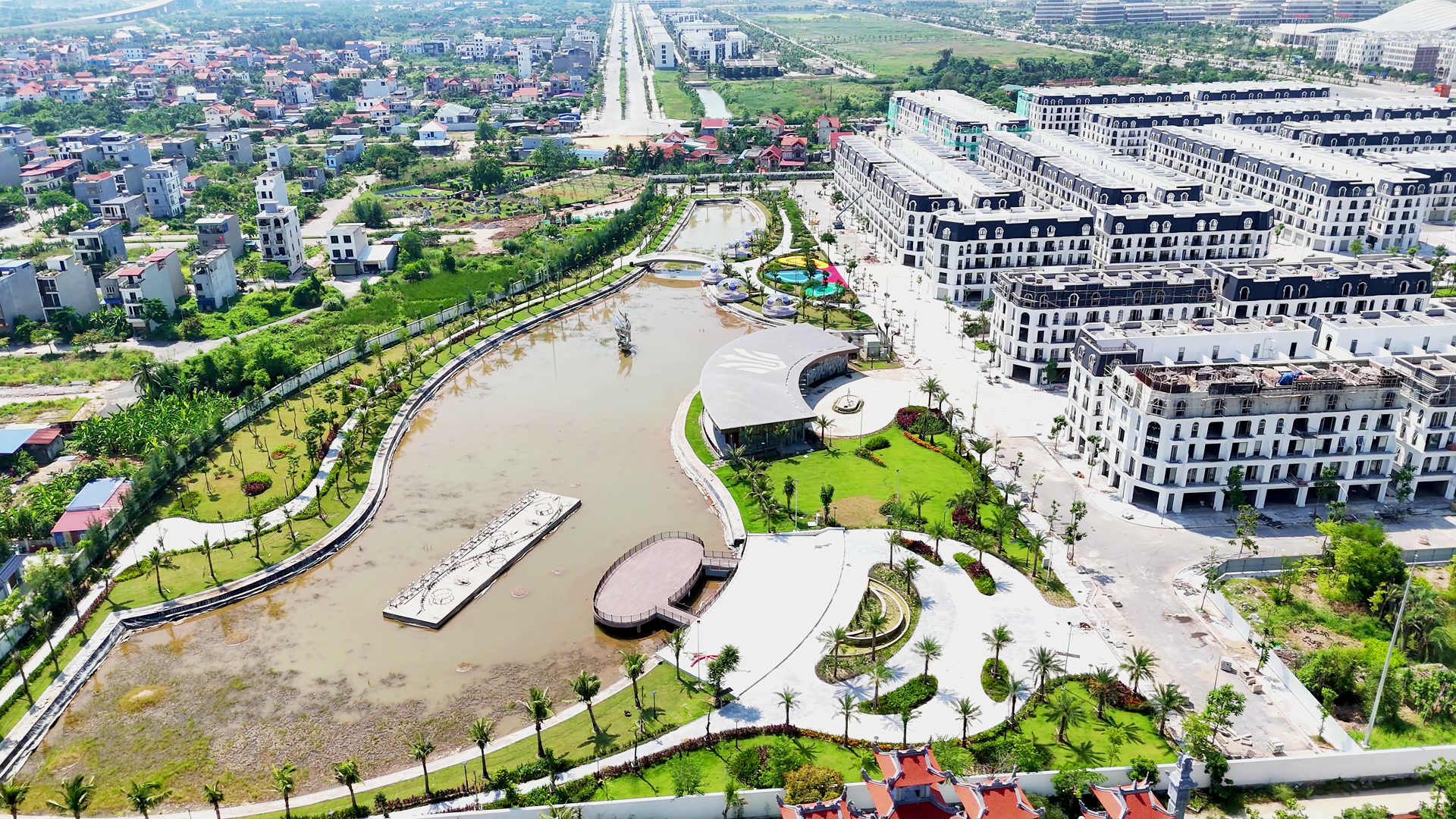 Hồ nước lớn trong Hoàng Huy New City, đường dạo và cây xanh chạy quanh hồ, nhà hàng ven hồ mái tròn, phía sau là các dãy nhà phố đang hoàn thiện