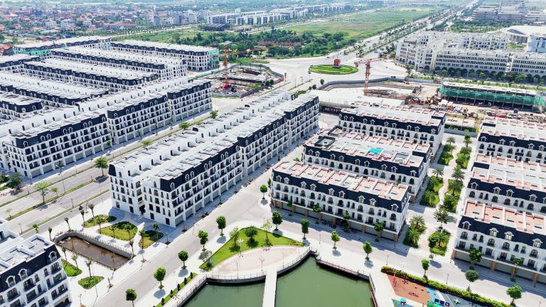 Toàn cảnh một góc Hoàng Huy New City tháng 10/2026, các dãy nhà phố mặt trắng mái đen quanh công viên hồ, phía xa còn cần cẩu đang làm