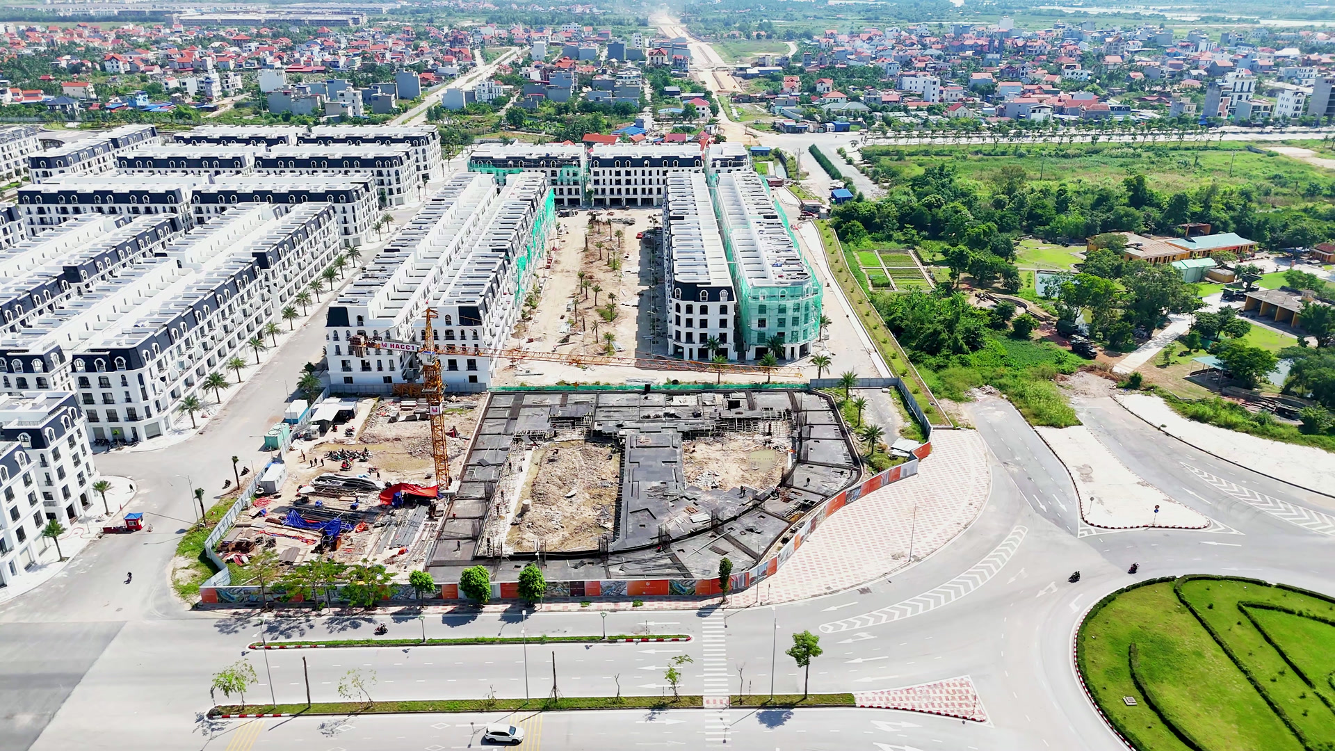 Ô đất đang làm móng sát vòng xuyến ở Hoàng Huy New City, vành móng bê tông chạy theo mép cong của ô đất, bên trong là các ô móng và cần cẩu, xung quanh là dãy nhà phố đã xây
