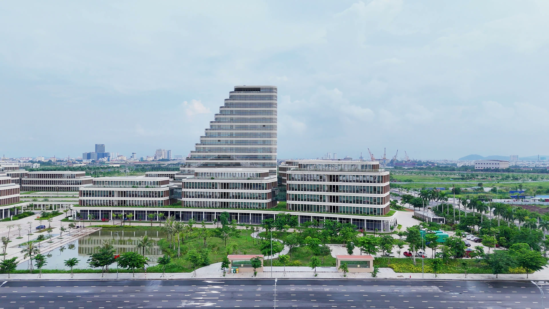 Một khối nhà của Trung tâm Chính trị – Hành chính thành phố Hải Phòng ở Bắc Sông Cấm, toà tháp bậc thang ở giữa và các khối thấp tầng hai bên, phía trước là hồ nước, cây xanh và đường lớn