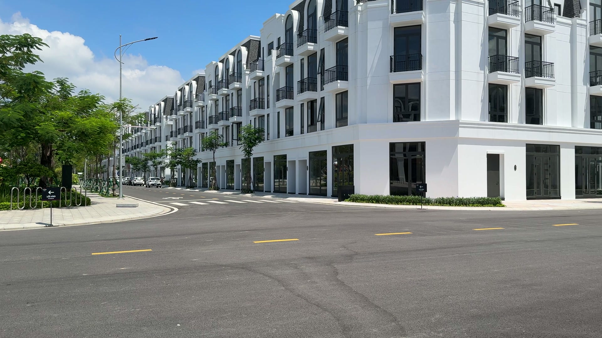 Dãy nhà phố bốn tầng sơn trắng đã xây xong mặt ngoài ở góc ngã tư trong khu đô thị, đường nhựa kẻ vạch vàng không có người qua lại