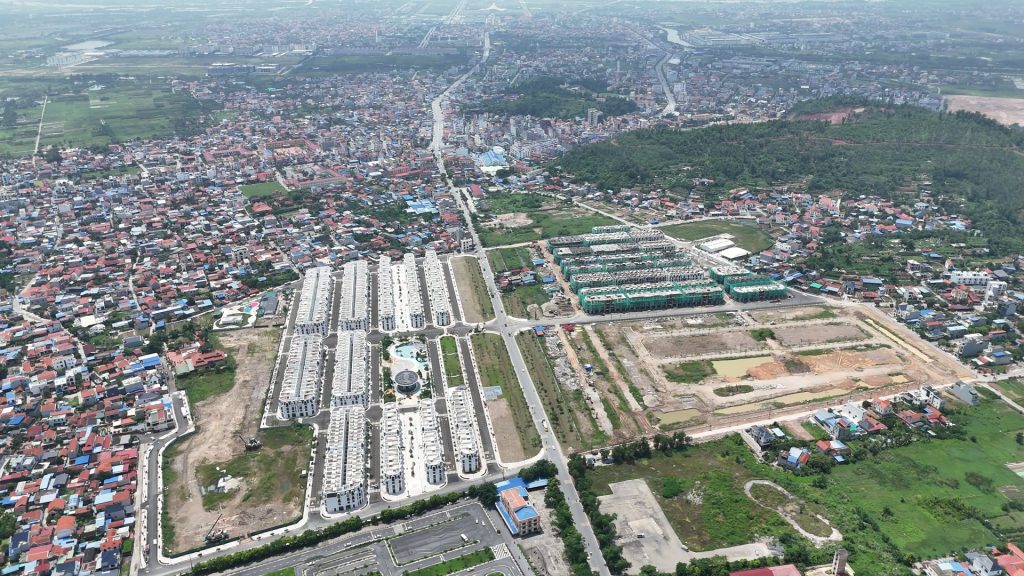 Toàn cảnh khu đô thị Vlasta Thủy Nguyên nhìn từ trên cao, các dãy nhà thấp tầng màu trắng nằm giữa khu dân cư dày đặc, cạnh đó là các lô đất còn trống và đồi cây xanh phía sau