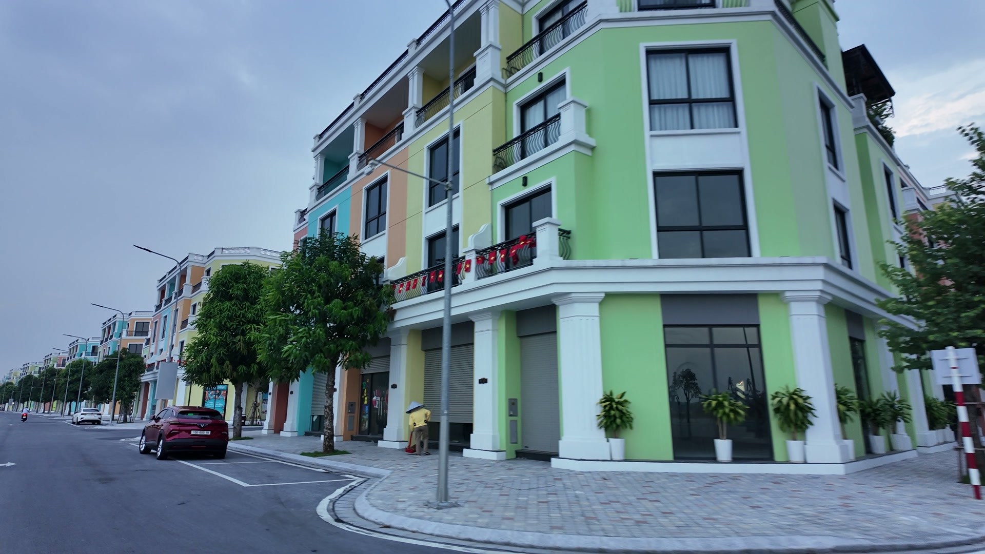 Dãy nhà phố bốn tầng trên đảo Vũ Yên, mỗi căn sơn một màu xanh lá, cam, xanh ngọc, vàng kem, hàng cây và cột đèn chạy dọc vỉa hè
