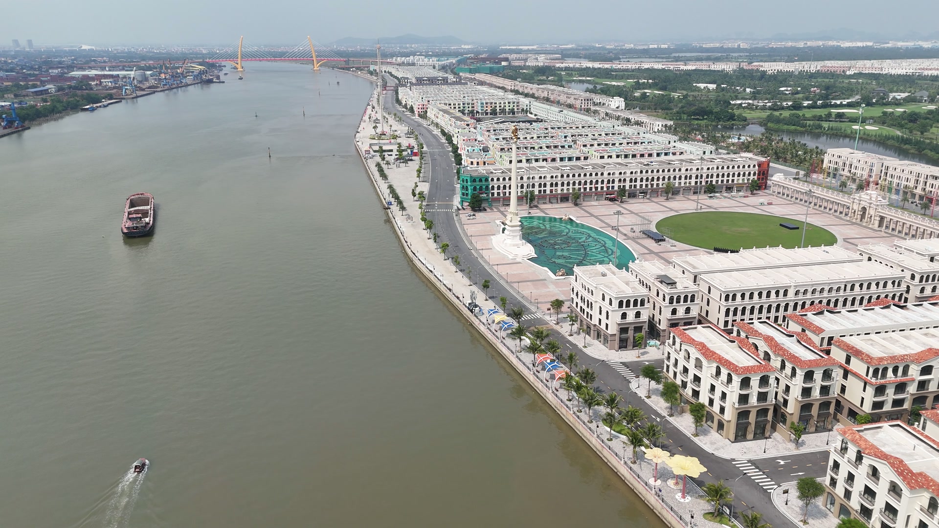 Quảng trường Châu Âu trên đảo Vũ Yên ven sông Cấm, cột tháp trắng đỉnh vàng đứng cạnh hồ nước xanh ngọc, bên cạnh là bãi cỏ bầu dục, dãy nhà trắng có vòm cuốn, phía xa là cầu Hoàng Gia với hai trụ tháp vàng