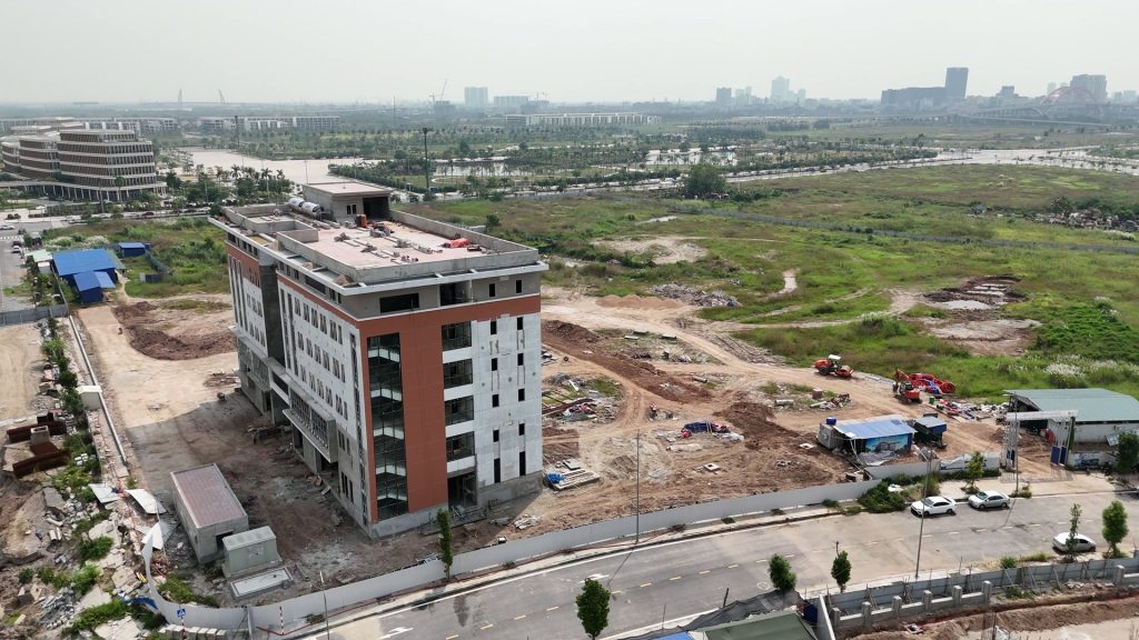 Thủy Nguyên nhìn từ trên cao, toà nhà sáu tầng của tổ hợp giáo dục EQuest ở Bắc Sông Cấm giữa bãi đất trống và đường nội bộ, phía xa là các khu nhà cao tầng