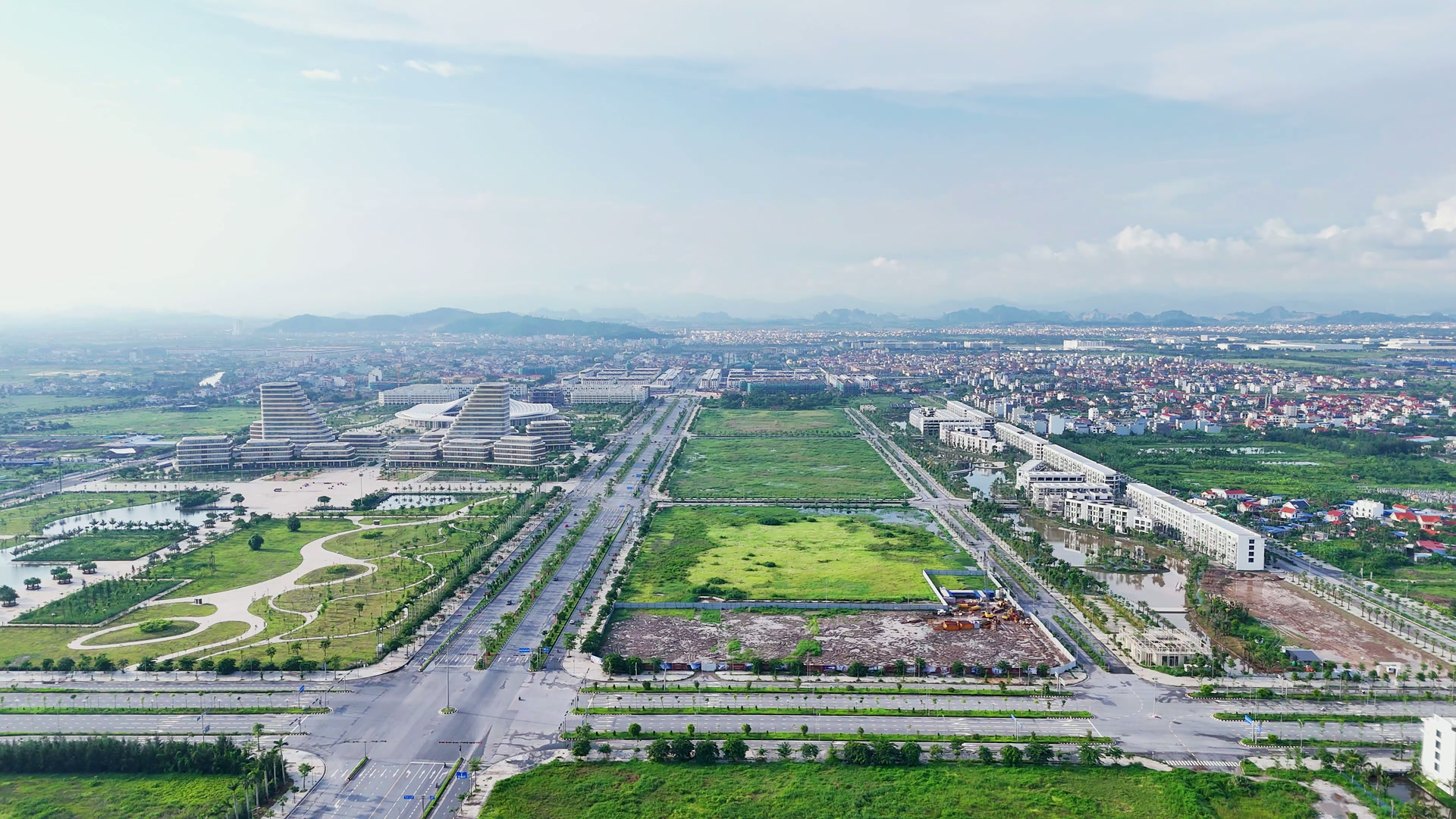 Trục đường lớn mới mở ở Bắc Sông Cấm, hai bên là những ô đất còn để cỏ và một ô đất đang san, xa xa là các khối nhà Trung tâm Chính trị – Hành chính và một dãy nhà phố mới