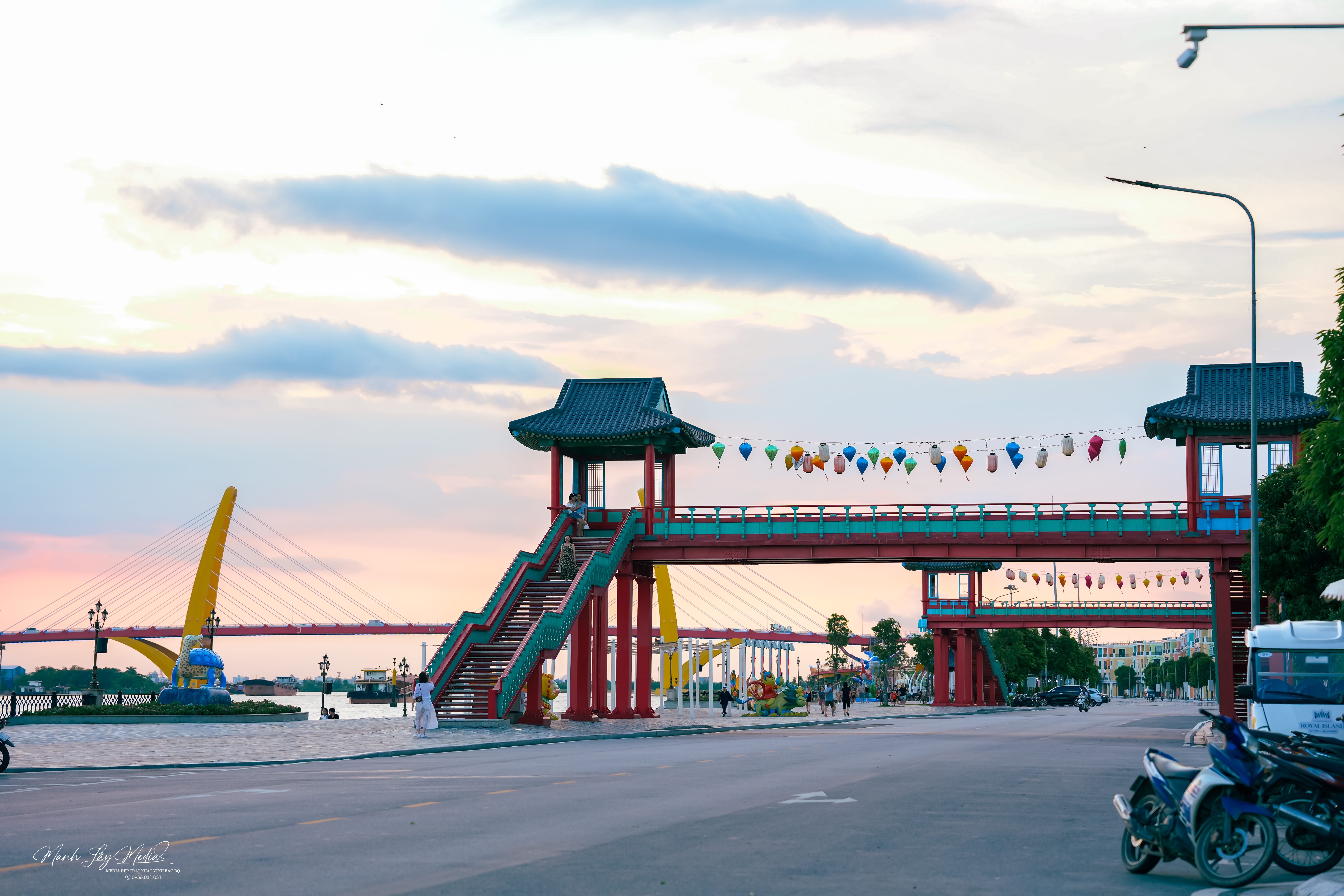 Khu phố đi bộ ven sông trên đảo Vũ Yên với cổng chào và cầu bộ hành trang trí đèn lồng, phía xa là cầu dây văng qua sông