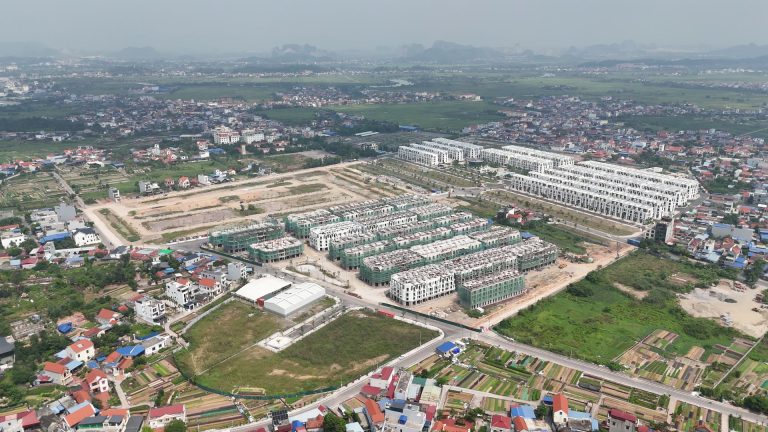 Toàn cảnh Vlasta Thủy Nguyên tháng 10/2026: các dãy nhà phố trắng đã hoàn thiện, các dãy còn quây lưới xanh và bãi đất đã chia ô, xung quanh là làng xóm và ruộng