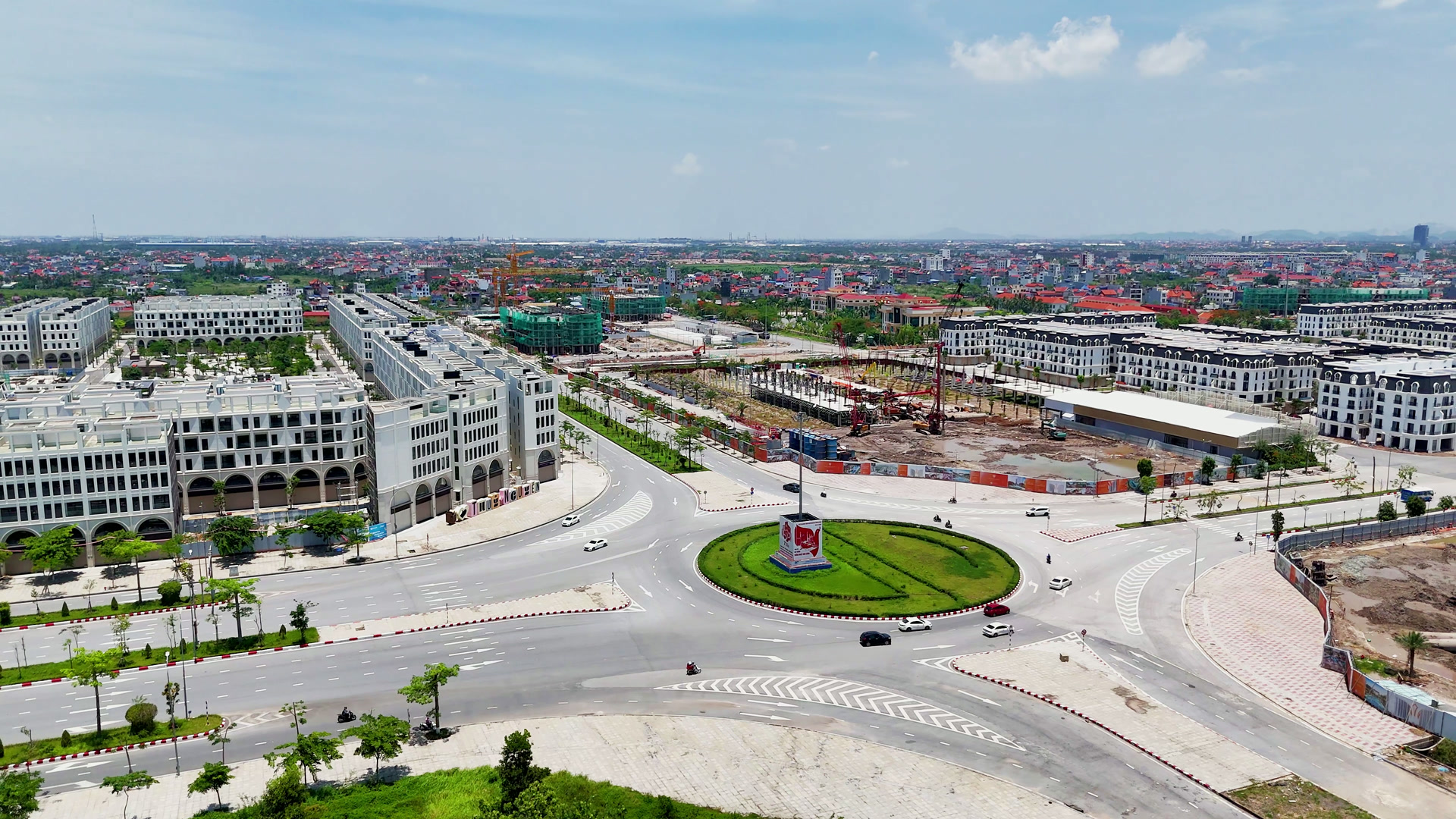 Vòng xuyến có bồn cỏ tròn trên một trục đường lớn ở Thủy Nguyên, một bên là dãy nhà phố mới nhiều tầng, một bên là công trường đang xây, xe cộ qua lại